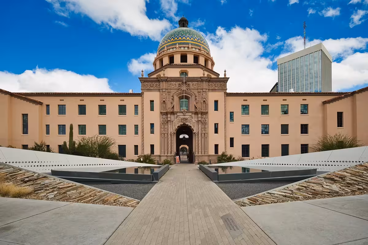 Historic building with colorful tiled dome and ornate arched entrance, brick walkway, blue sky.