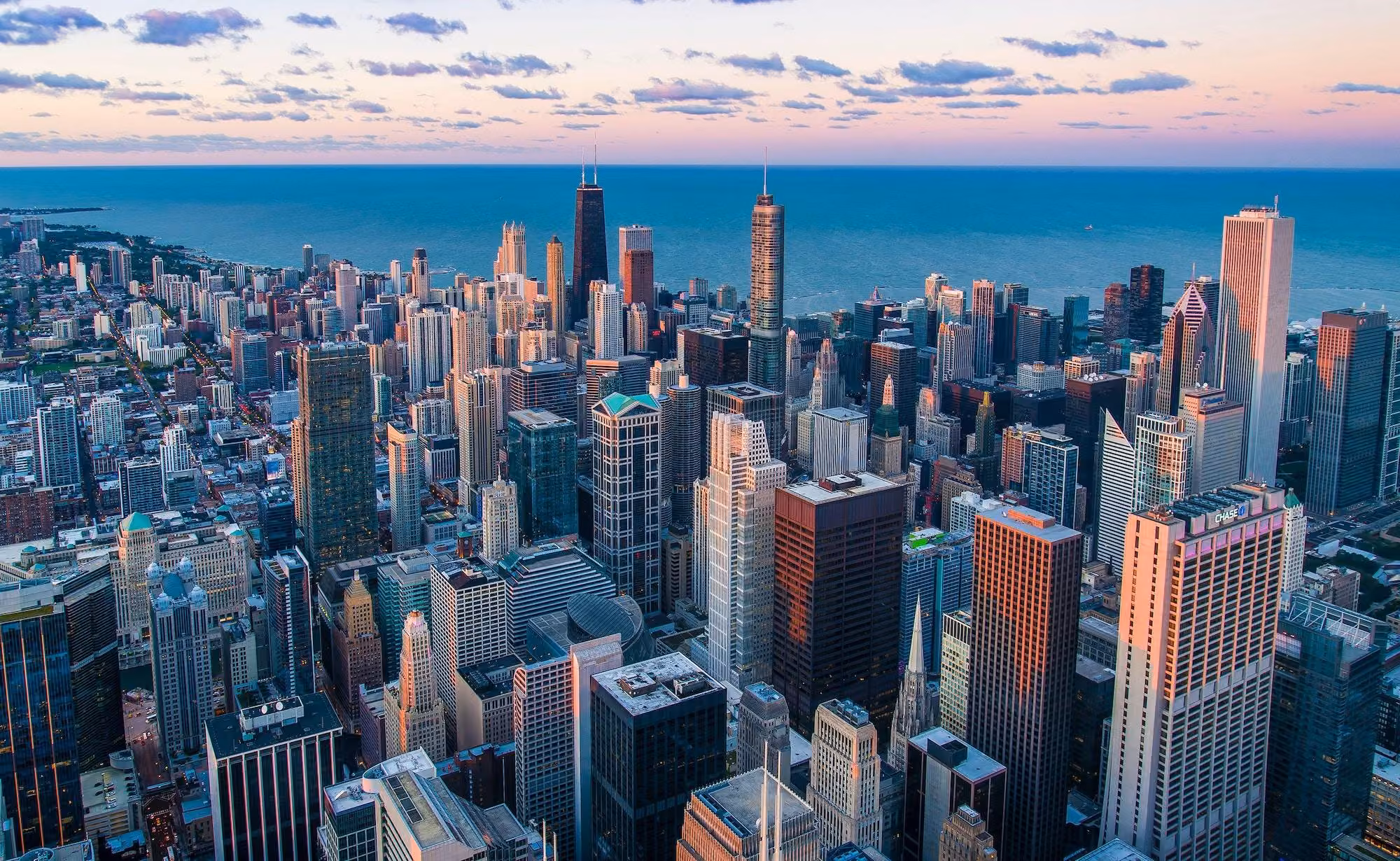 Downtown skyscrapers at dusk beside a calm lake, with a WGN sign visible on one building.