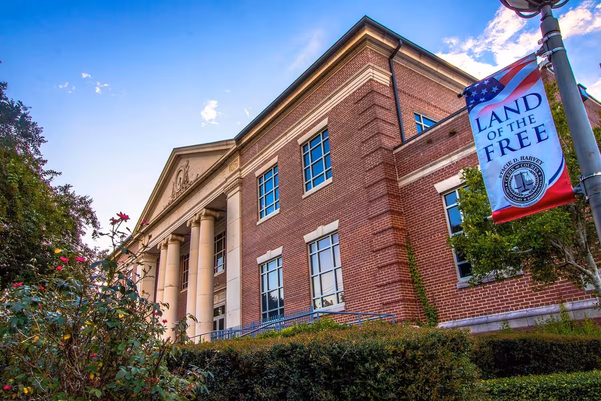 Brick courthouse with columns under blue sky; lamppost banner reads "Land of the Free" with a seal.