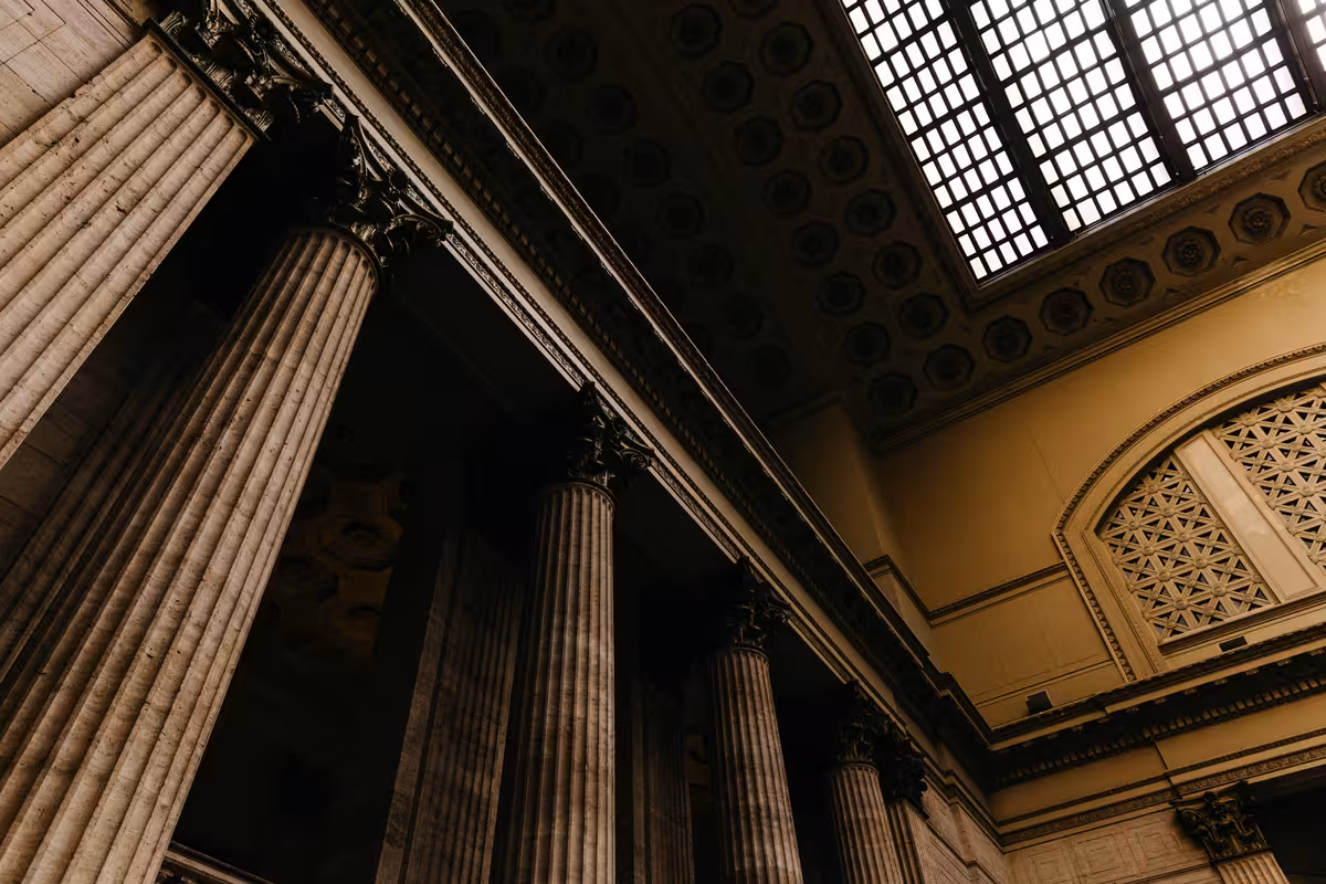 Tall marble columns and ornate coffered ceiling beneath a large grid skylight in a grand hall